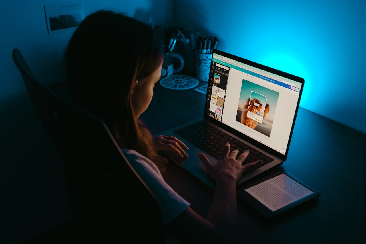 A girl uses a laptop at a desk in a dimly lit room, with a blue light creating a calm ambiance.